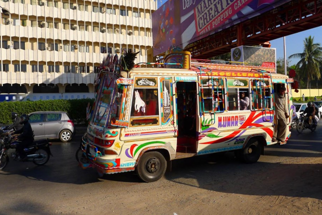 Traditional minibuses of Karachi public transport vehicles navigating through heavy traffic on a busy Karachi street.